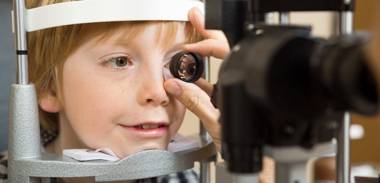 Closeup of male optician's hand checking boy's eye with lens in store